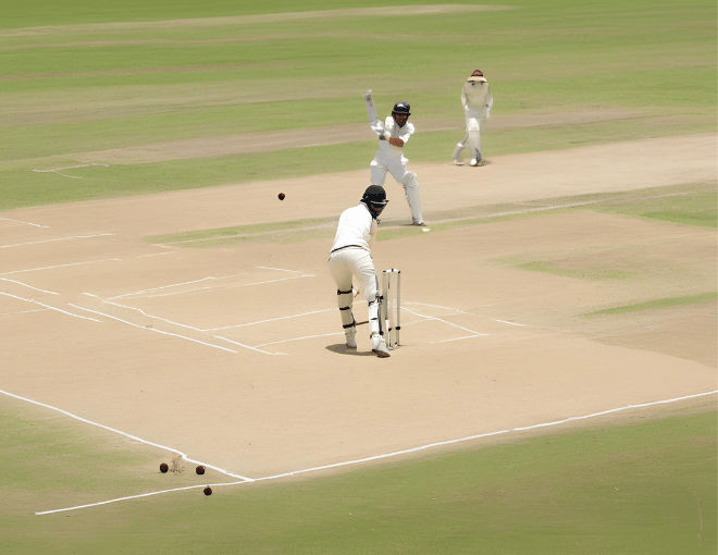 The cricket ball races across the pitch, dust rising from the ground, as the batsman narrowly avoids being bowled out.